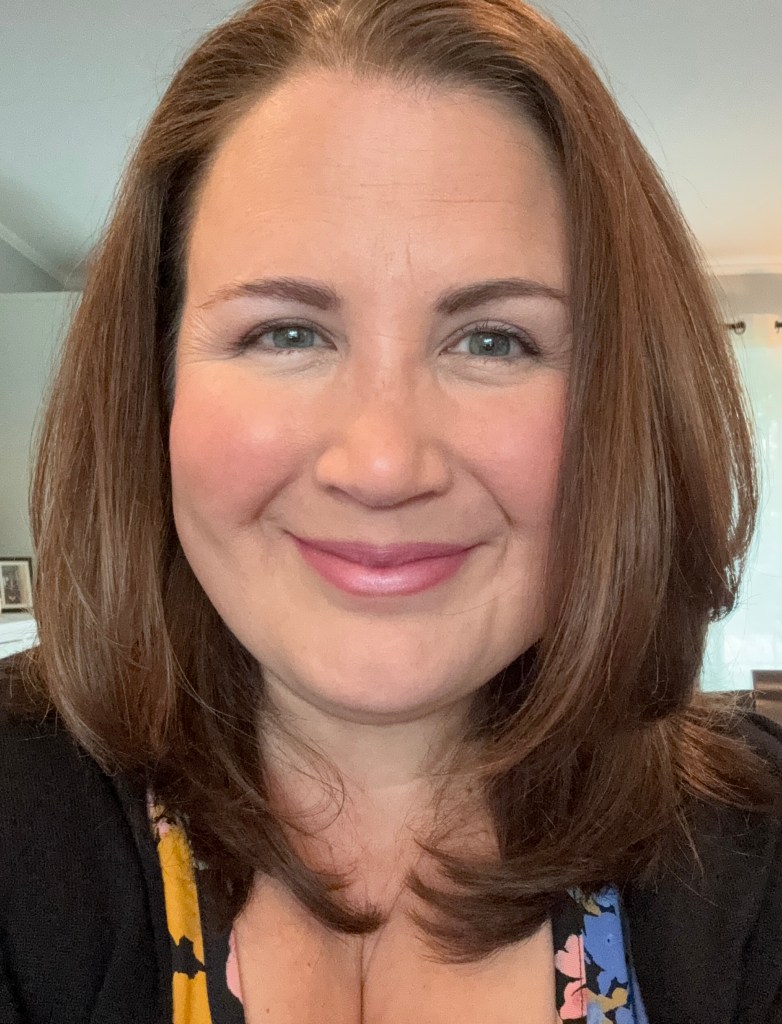 myself, a woman with long brown hair and green eyes, a black shirt with yellow and blue flowers, and a small smile
